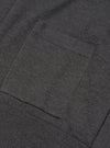Close-up detail of a charcoal merino cardigan showing a patch chest pocket with neat stitched edges and a ribbed hem band below. The fine-knit merino fabric has a smooth, dense texture in a dark grey marl. Shot flat against a plain background.