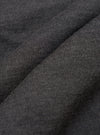 Close-up of charcoal merino knit fabric, showing a fine, even stocking stitch with a soft, slightly heathered texture. The fabric is gathered into soft folds, highlighting the drape and weight of the knit. No background is visible.
