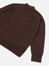 Flat lay of an espresso brown merino cardigan on a white studio surface, shot from above at an angle. The smooth fine-knit body shows raglan-style seam lines at the shoulder. A ribbed hem and ribbed cuff on the visible sleeve are clearly shown. A small collar is visible at the top of the frame.