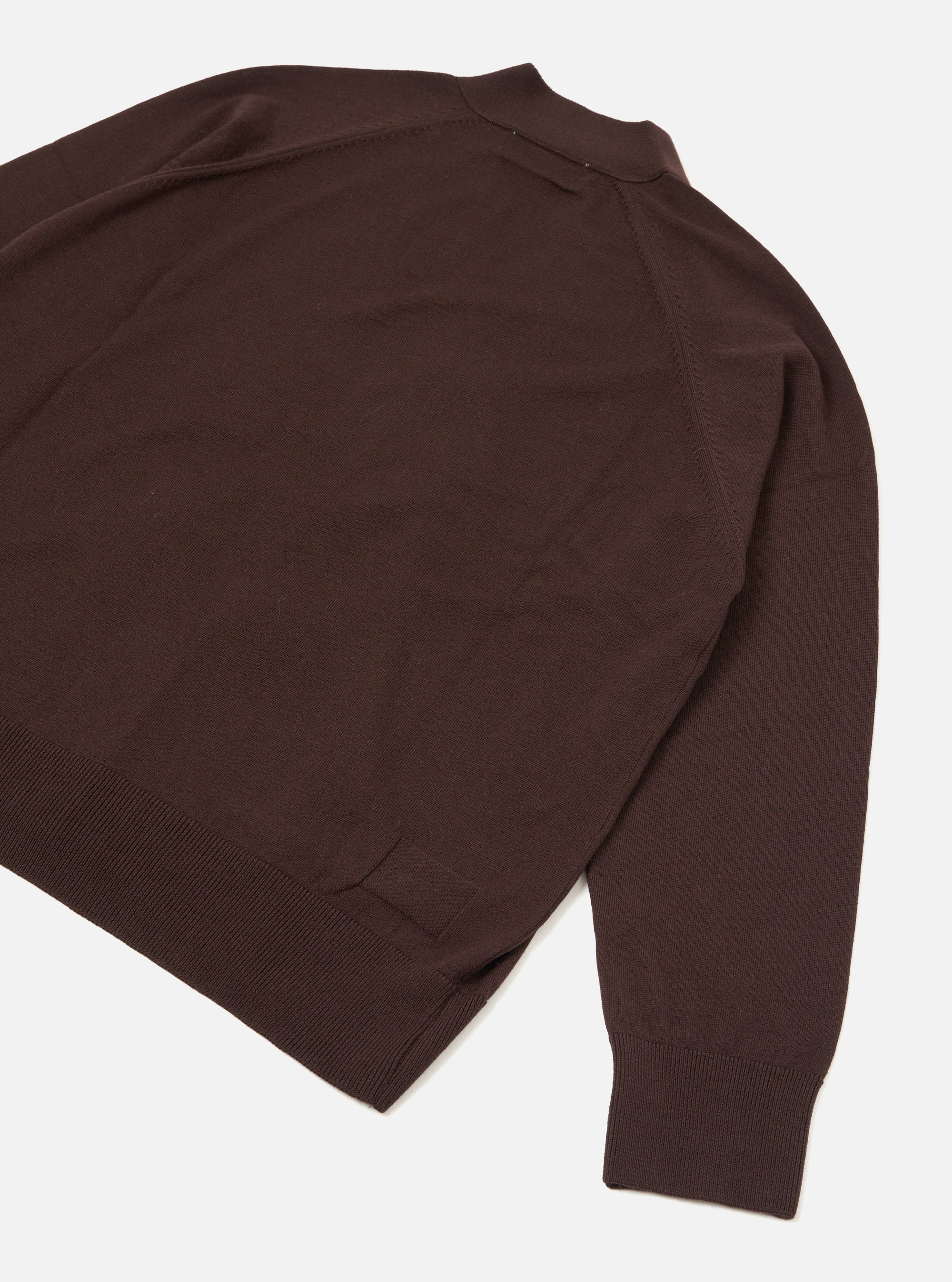 Flat lay of an espresso brown merino cardigan on a white studio surface, shot from above at an angle. The smooth fine-knit body shows raglan-style seam lines at the shoulder. A ribbed hem and ribbed cuff on the visible sleeve are clearly shown. A small collar is visible at the top of the frame.