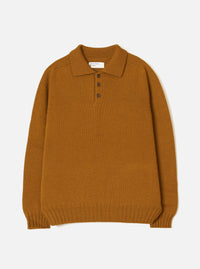 Gold Shetland knit polo sweater laid flat on a white studio backdrop. Features a spread collar, three-button placket with dark buttons, ribbed cuffs and hem, and a chunky plain knit texture throughout. A Universal Works woven label sits inside the collar.