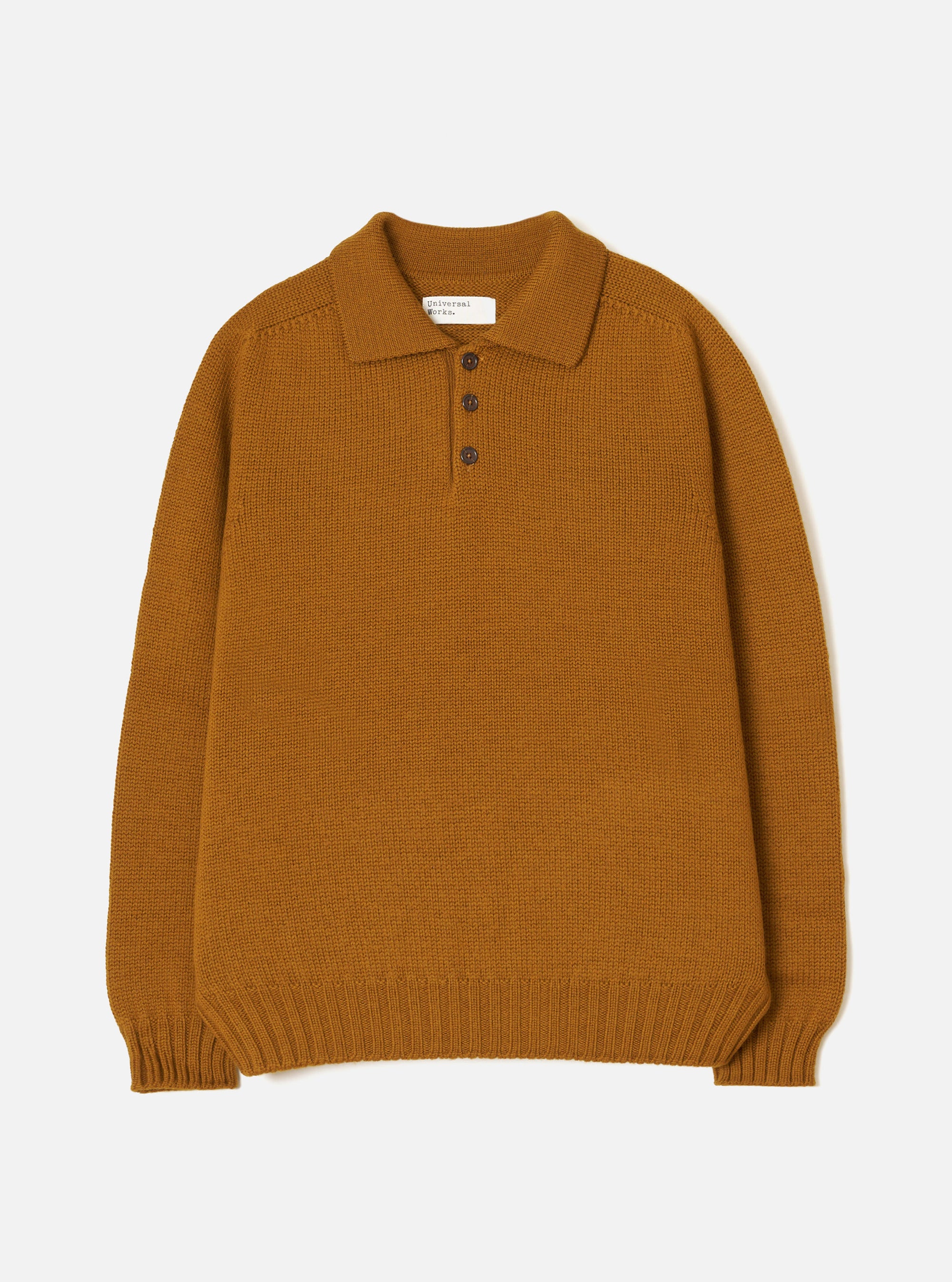 Gold Shetland knit polo sweater laid flat on a white studio backdrop. Features a spread collar, three-button placket with dark buttons, ribbed cuffs and hem, and a chunky plain knit texture throughout. A Universal Works woven label sits inside the collar.
