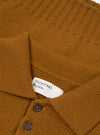Close-up flat lay of a gold Shetland knit Curtis sweater by Universal Works. The spread collar and upper button placket are shown, with two dark horn-effect buttons visible. A white woven brand label reads "Universal Works." The knit texture varies between plain and ribbed sections across the body.