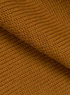 Close-up detail shot of the gold Shetland knit fabric on the Curtis sweater. The chunky knit texture is clearly visible, showing individual yarn loops in a warm amber-gold tone. A folded section runs diagonally across the frame, highlighting the fabric's depth and softness.