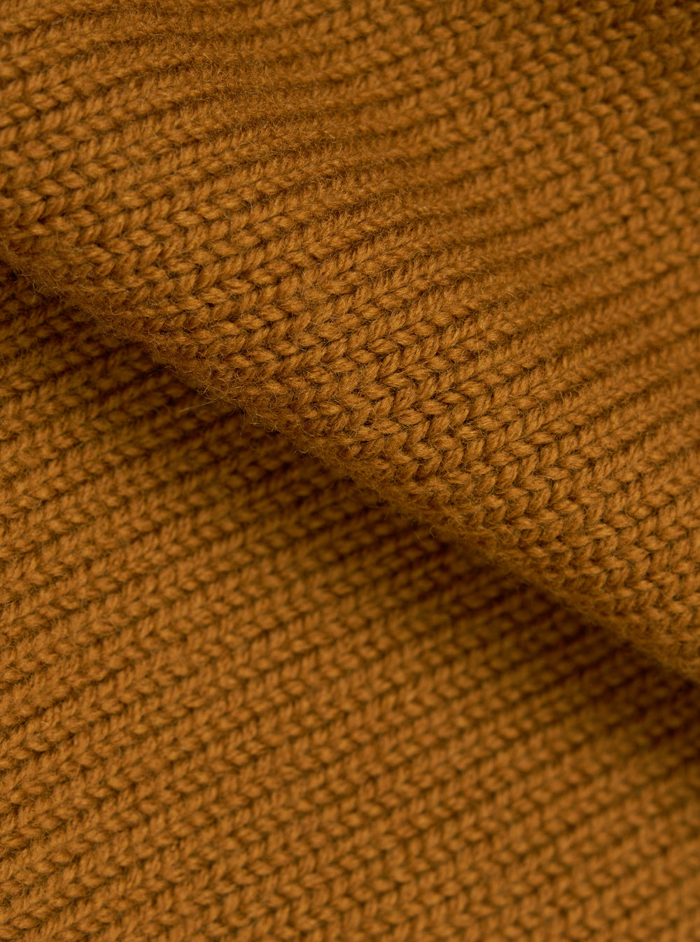 Close-up detail shot of the gold Shetland knit fabric on the Curtis sweater. The chunky knit texture is clearly visible, showing individual yarn loops in a warm amber-gold tone. A folded section runs diagonally across the frame, highlighting the fabric's depth and softness.