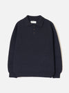 Navy Shetland knit polo sweater laid flat on a light grey seamless backdrop. Features a spread collar, three-button placket with dark buttons, chunky textured knit body, long sleeves, and a wide ribbed hem and cuffs. A Universal Works woven label is visible at the collar.