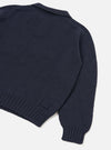 Navy Shetland knit polo sweater shot flat on a light grey seamless backdrop, angled to show the back and one sleeve. The body features a textured stocking-stitch knit with ribbed side panels, ribbed hem and ribbed cuffs. A spread collar is visible at the top. The sleeve seam shows a neat linking stitch detail.