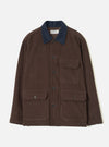 Cacao brown corduroy utility jacket laid flat on a light grey backdrop. Features a contrast navy corduroy collar, five dark buttons down the front placket, one buttoned chest patch pocket, and two large buttoned patch pockets at the hip. A Universal Works woven label sits inside the collar.