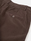 Close-up detail of cacao brown corduroy military chino trousers on a white studio backdrop. The wide-wale cord texture is clearly visible. A single welt back pocket with a four-hole button fastening is shown, alongside a belt loop and waistband at the top of the frame.