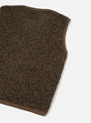 Close-up flat lay of a brown boucle style fleece gilet on a white studio backdrop. The dense, curly-textured fleece body is trimmed with smooth brown fabric binding along the armhole and hem edges. The shot is cropped to show the front panel, shoulder, and lower hem corner.