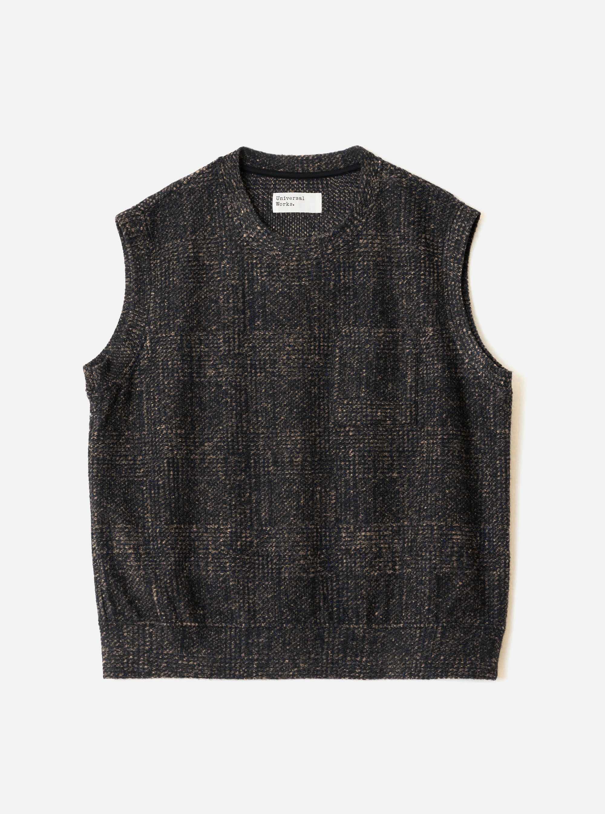 Navy sleeveless crew-neck knit vest laid flat on a light grey surface. The textured fabric features a muted check pattern in navy and tan. A Universal Works woven label sits inside the crew neck. The armholes are wide and the hem is straight and ribbed.