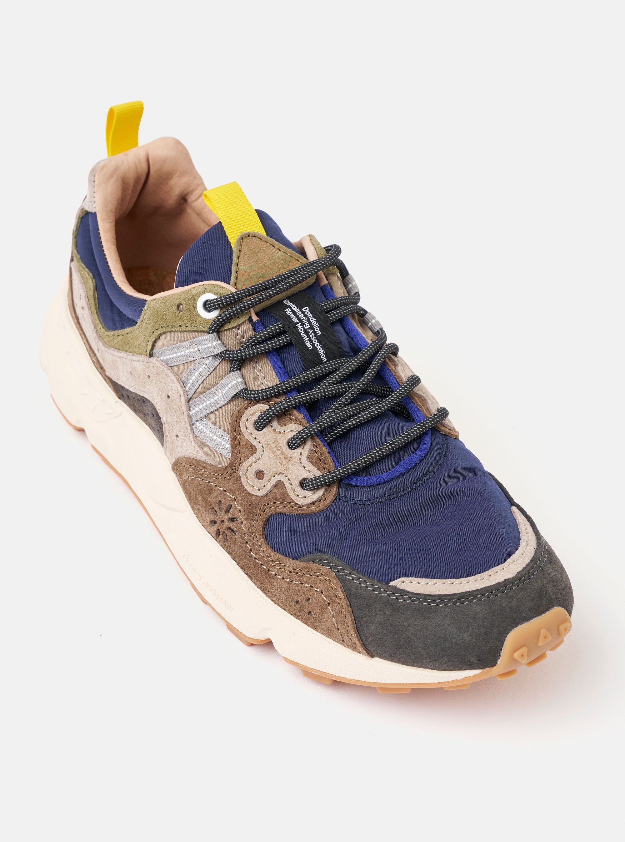 The Flower Mountain Dark Grey/Brown Suede/Nylon Yamano 3 Man is shown from a rear three-quarter angle in a studio shot against a plain white background. The sneaker features a dark grey and brown color palette with overlapping suede and nylon panels, a toothed rubber outsole, and trekking-style laces. A prominent heel tab and decorative stitching are visible.