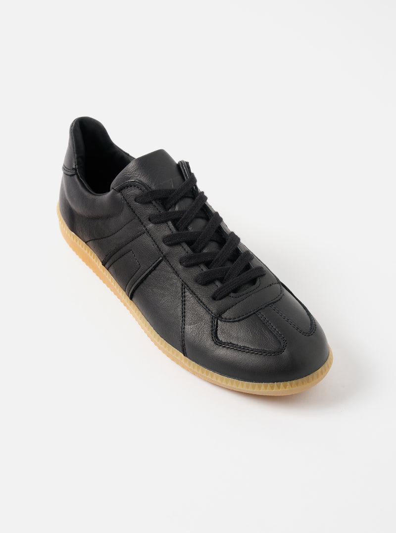 Studio shot of a Novesta for Universal Works Black Leather German Army Trainer on a white background. The shoe has black laces and a gum sole.