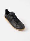 Studio shot of a Novesta for Universal Works Black Leather German Army Trainer on a white background. The shoe has black laces and a gum sole.