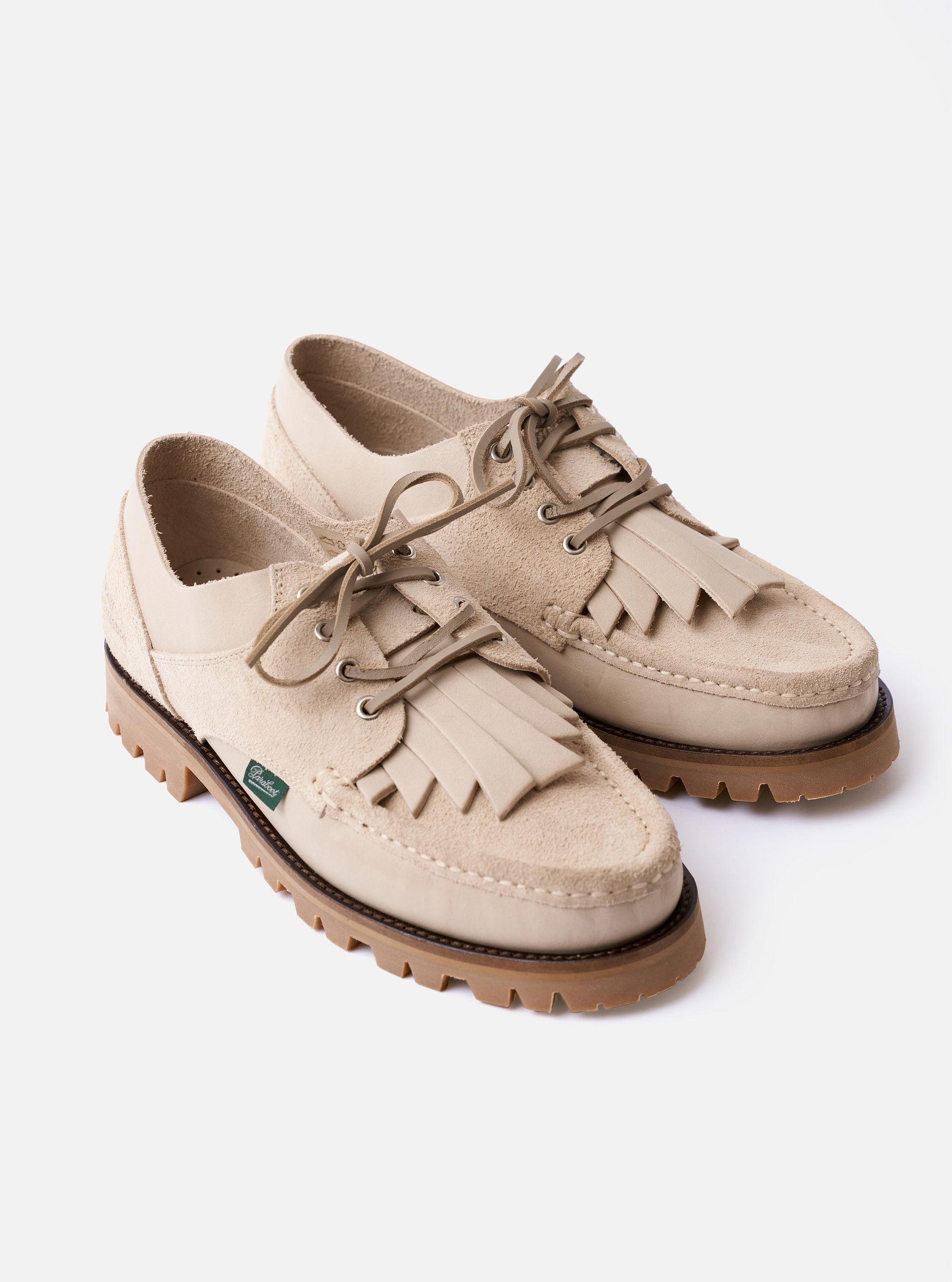 The Paraboot x Universal Works Thiers/Jannu in Sand Leather/Suede is shown from a rear three-quarter angle in a studio shot against a plain white background. The image highlights the contrast between the smooth sand-colored leather and the textured suede-like reverse on the heel and sides. It features a thick, vulcanized natural rubber sole with visible Blake stitch construction and piped seams along the collar.