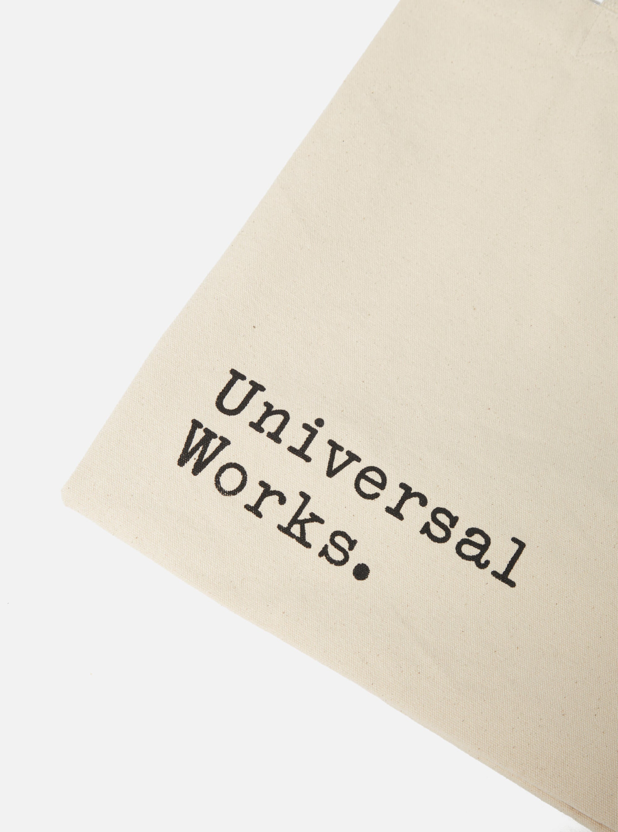 Close-up of an ecru Cotton Canvas Tote Bag on a white background. The bag features black text that reads "Universal Works."