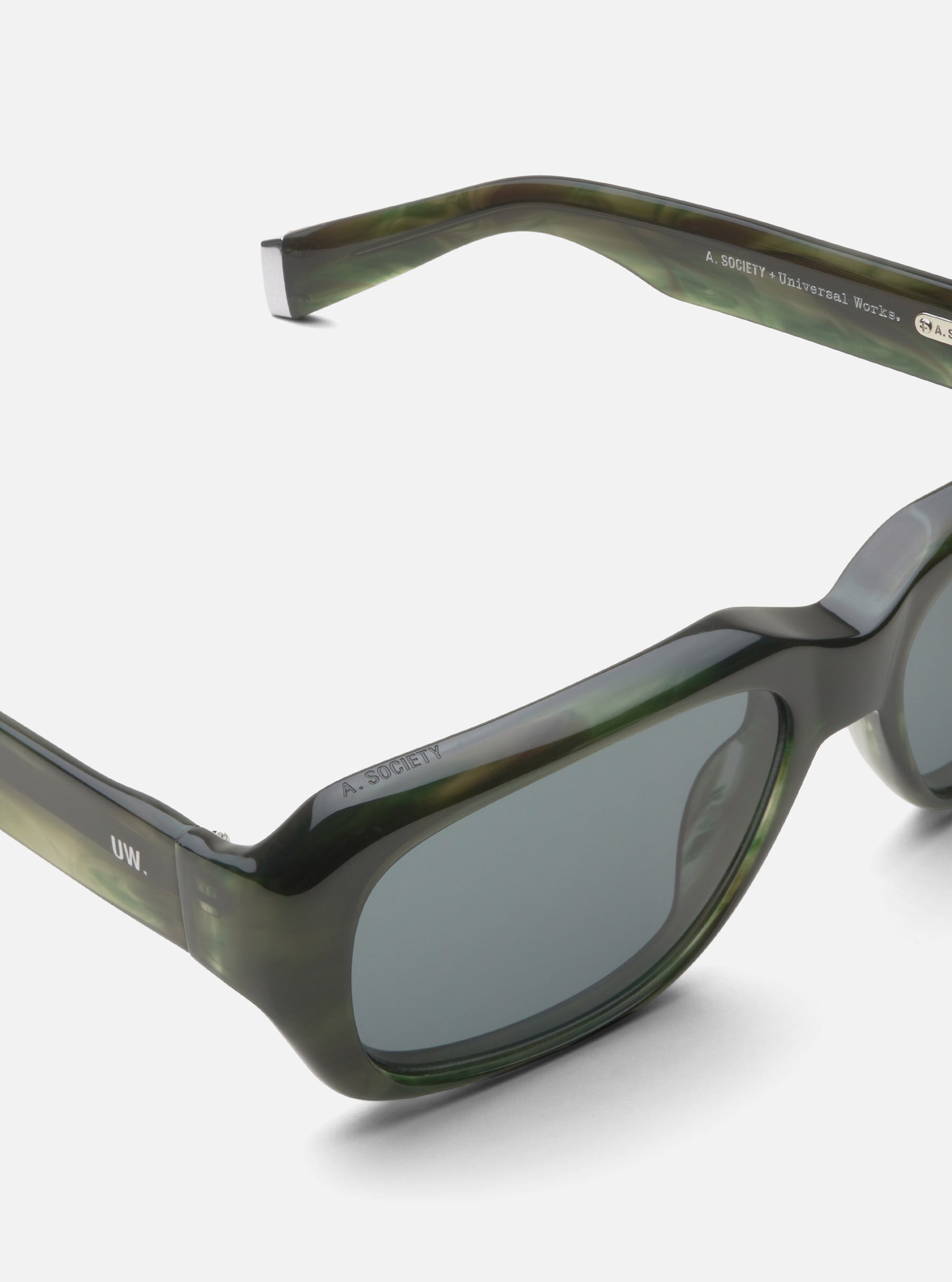 Close-up of A. SOCIETY x Universal Works Green Aberdeen Sunglasses on a white surface. The green marbled frames and grey lenses are clearly visible.