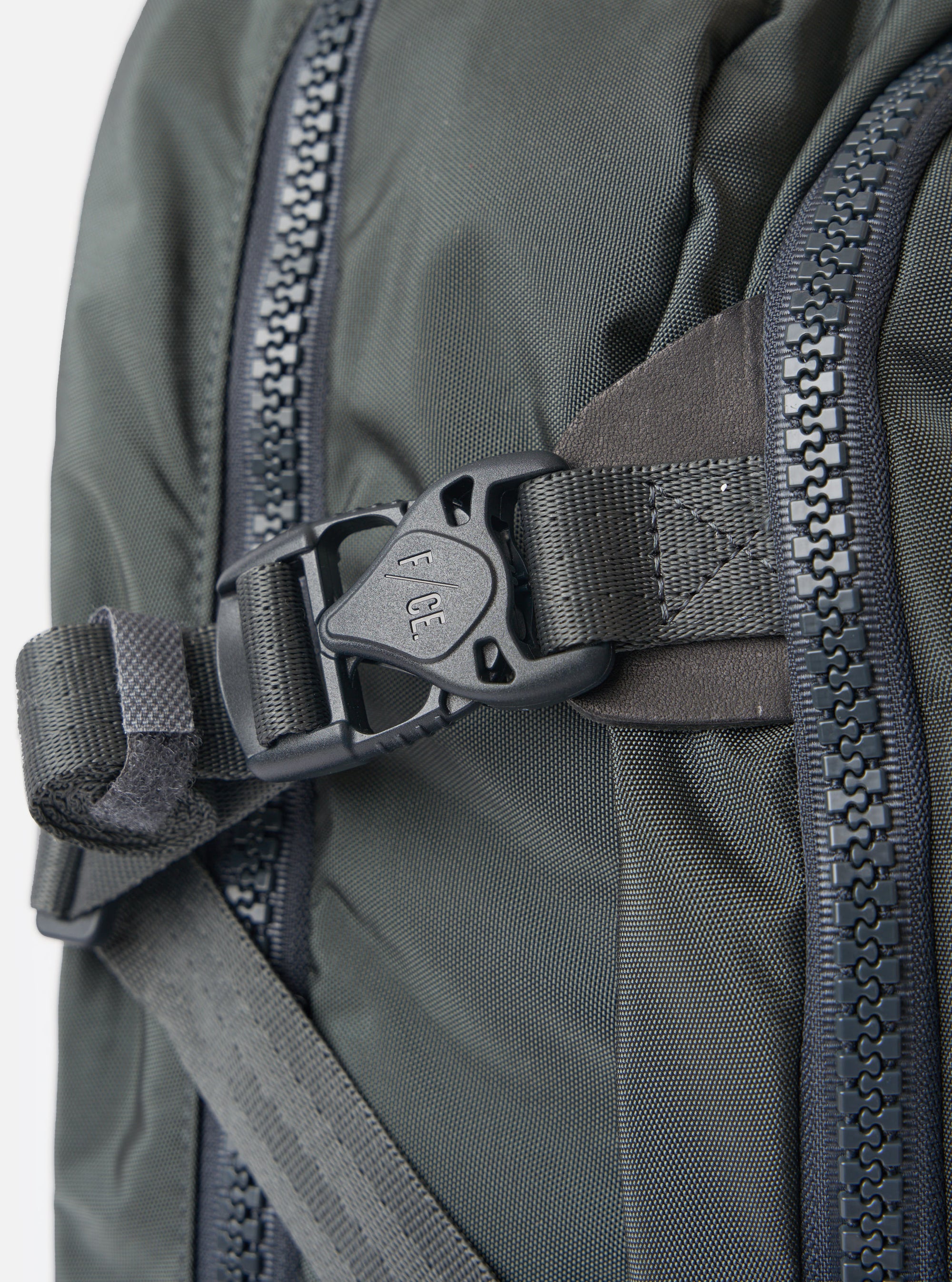Close-up of the F/CE.® Grey Recycled Nylon 420 re/cor Travel Backpack, showcasing the grey nylon material, heavy-duty zipper, and branded buckle against a plain white backdrop.