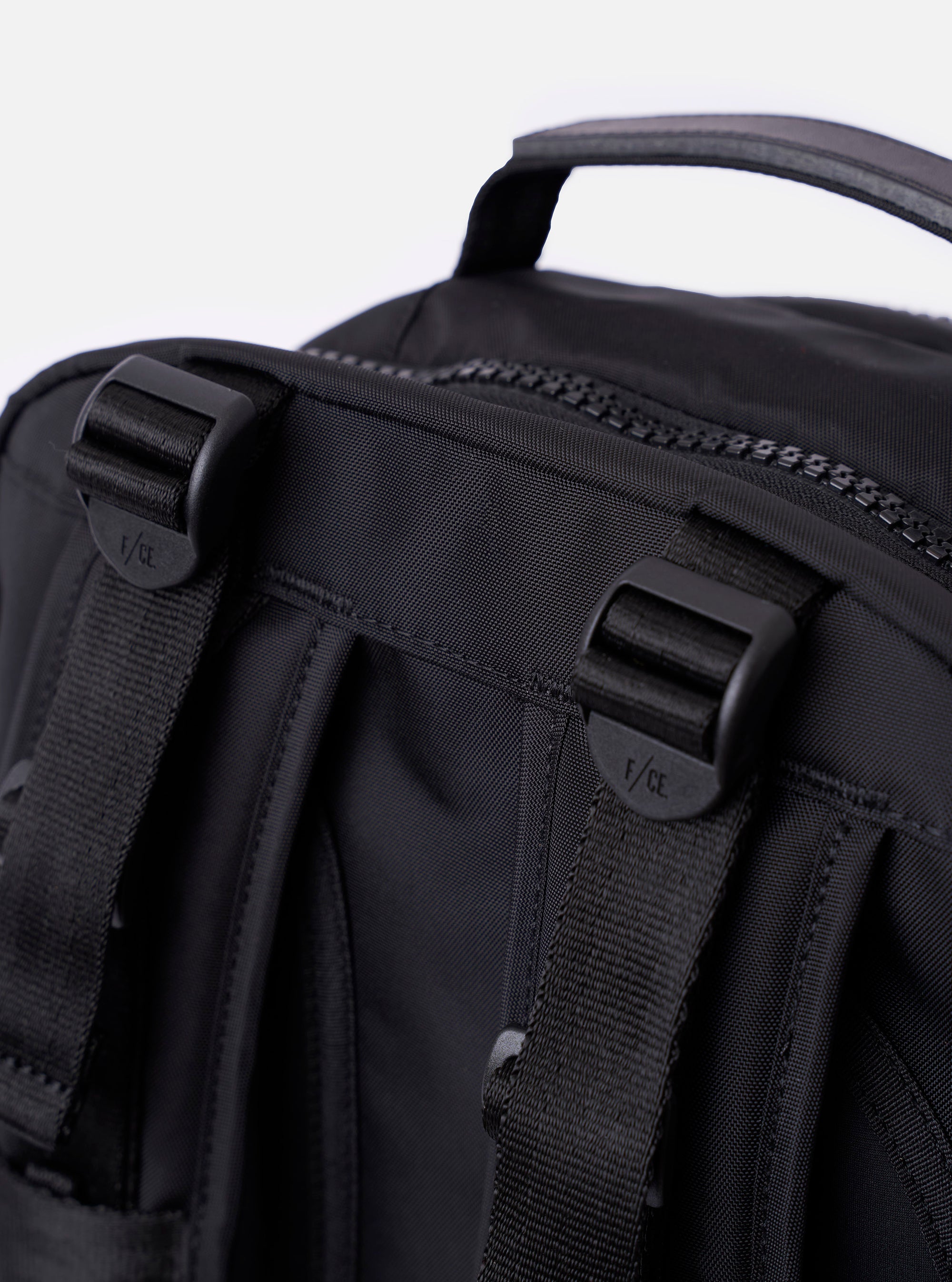 The F/CE.® Black Recycled Nylon 420 re/cor Travel Backpack is shown from a rear angle, highlighting the padded back panel made of black neoprene and the ergonomic shoulder straps. The straps feature the Mounting T System with nylon webbing for attachments and an adjustable chest buckle. The backpack is displayed as a flat lay against a plain white background.