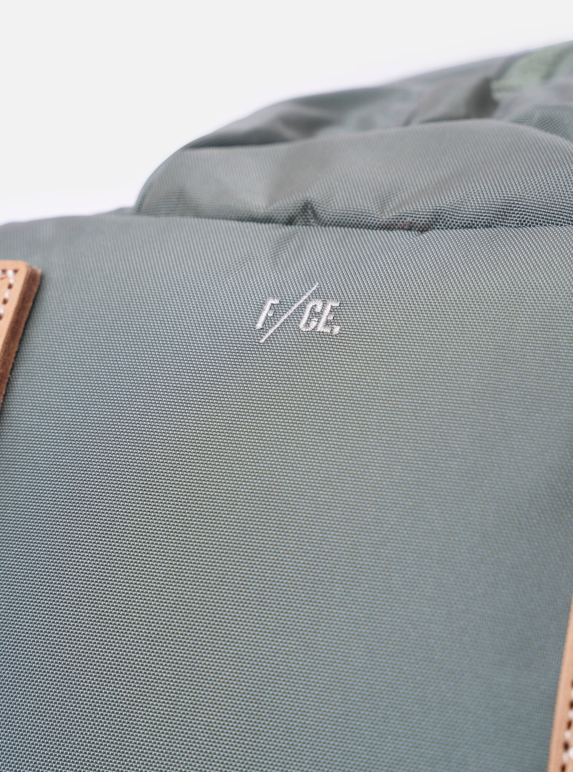 The F/CE.® Foliage Green Recycled Nylon 420 re/cor Travel Backpack is shown from a rear angle against a plain white background. This view highlights the ergonomic shoulder straps equipped with the MOUNTING T SYSTEM and a padded back panel made of technical neoprene. The foliage green recycled nylon fabric has a subtle sheen, and the adjustable straps and top handle are clearly visible.