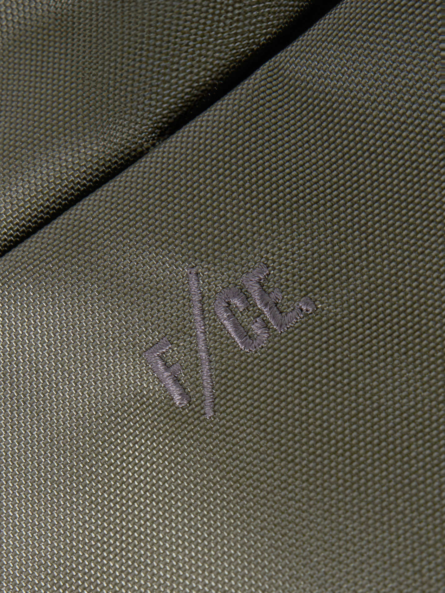 Close-up of the F/CE.® Sage Green 420 re/cor Sacoche. The sage green fabric shows a tight weave. The F/CE logo is embroidered in a matching thread. Studio shot.