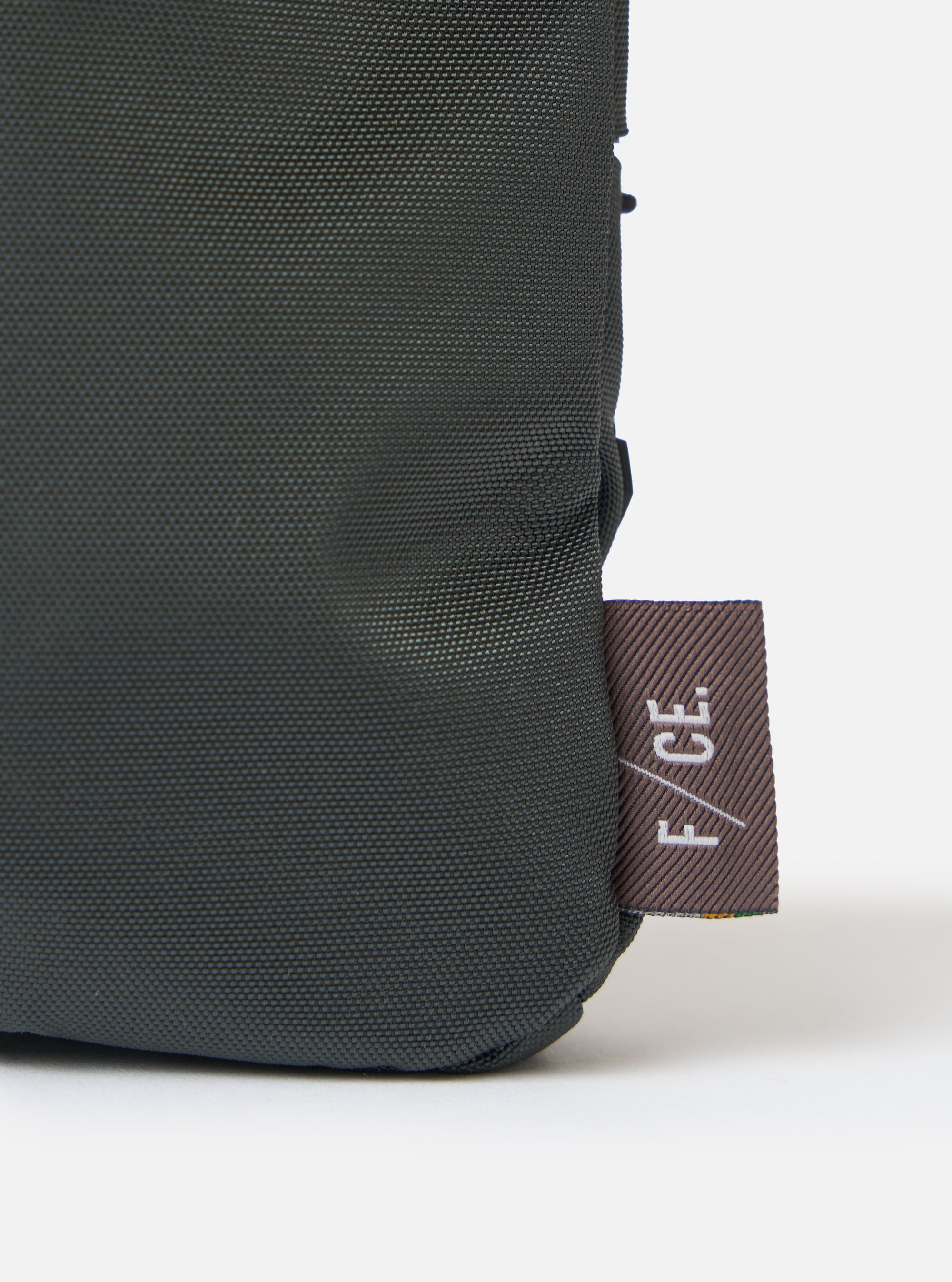 Close-up of the F/CE.® Grey 420 re/cor Sacoche showing the material texture and logo tag on a white background. The sacoche is a dark grey color.