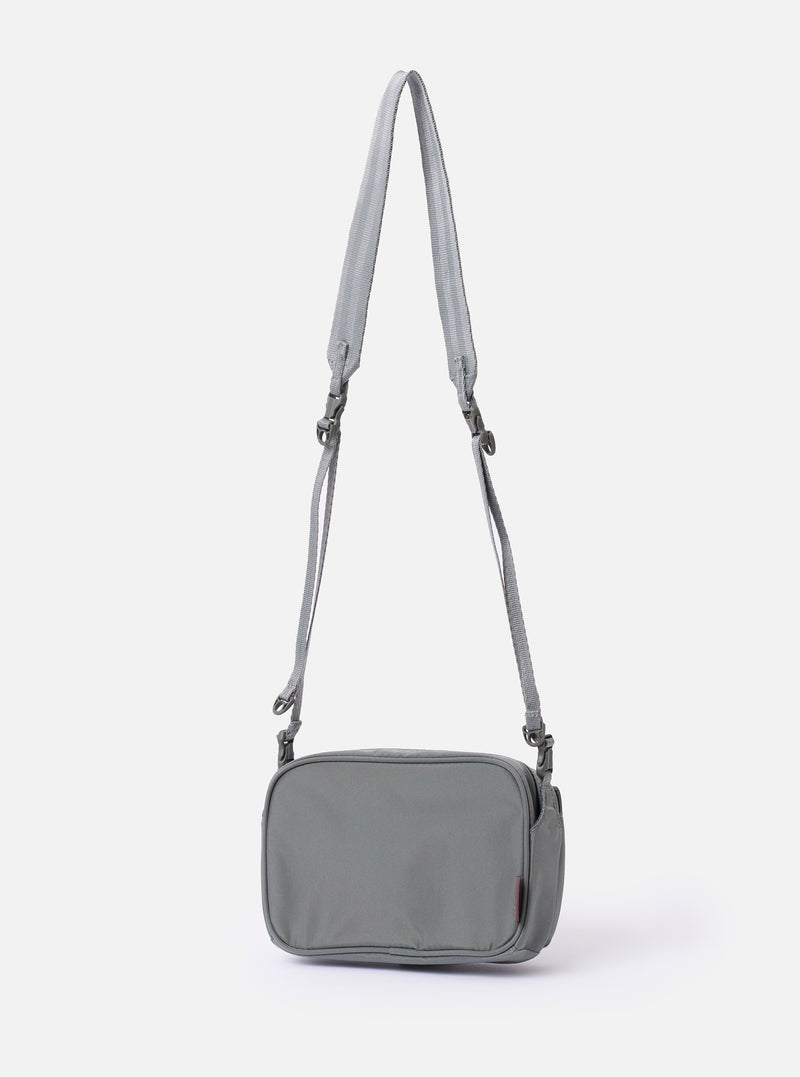 The F/CE. Foliage Green Recycled Nylon 420 re/cor Holiday Sacoche is shown from a rear angle as a flat lay against a plain white background. The image highlights the adjustable webbing shoulder strap with a plastic buckle and the clean back panel of the small, foliage green bag.