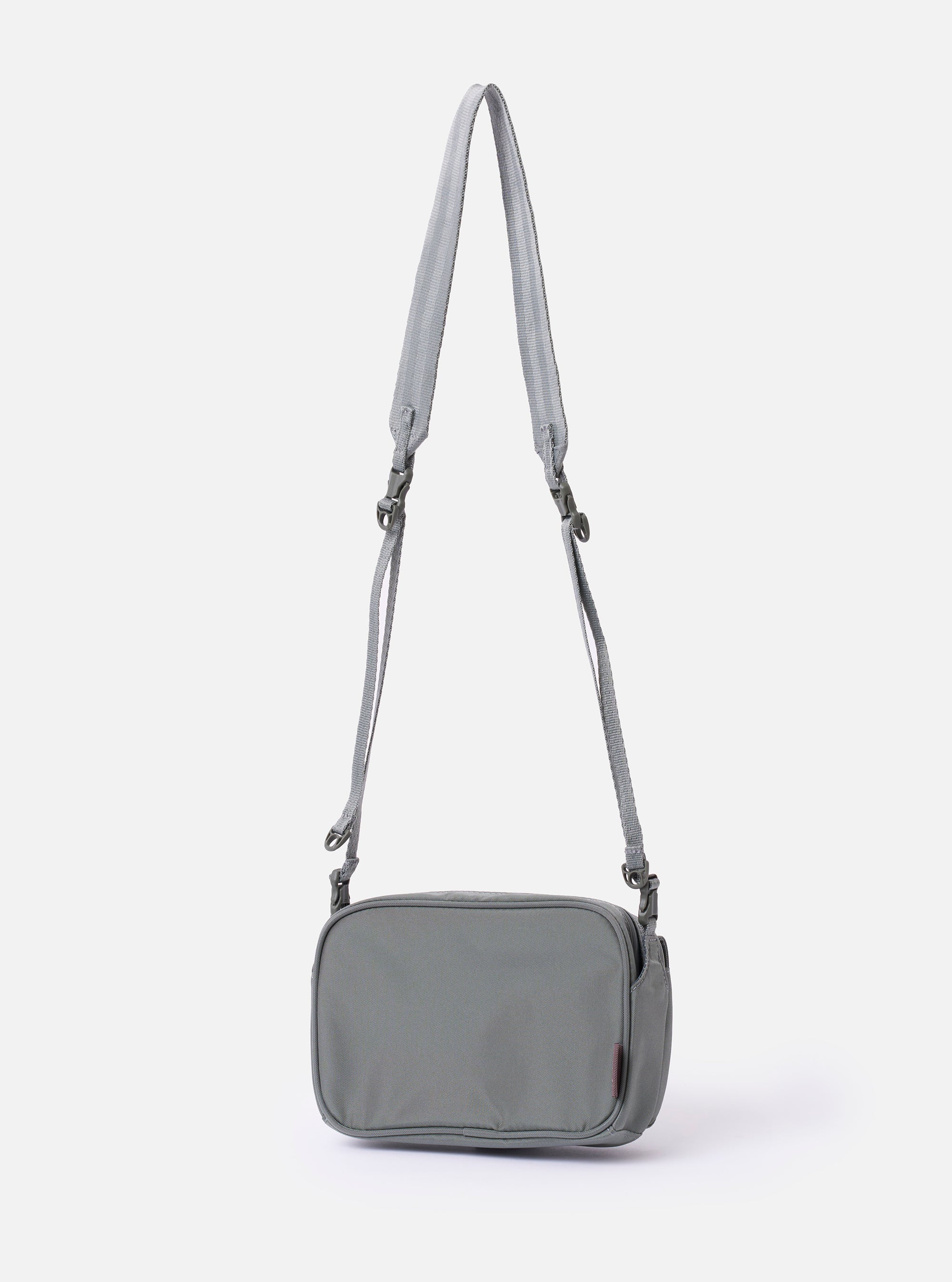 The F/CE. Foliage Green Recycled Nylon 420 re/cor Holiday Sacoche is shown from a rear angle as a flat lay against a plain white background. The image highlights the adjustable webbing shoulder strap with a plastic buckle and the clean back panel of the small, foliage green bag.