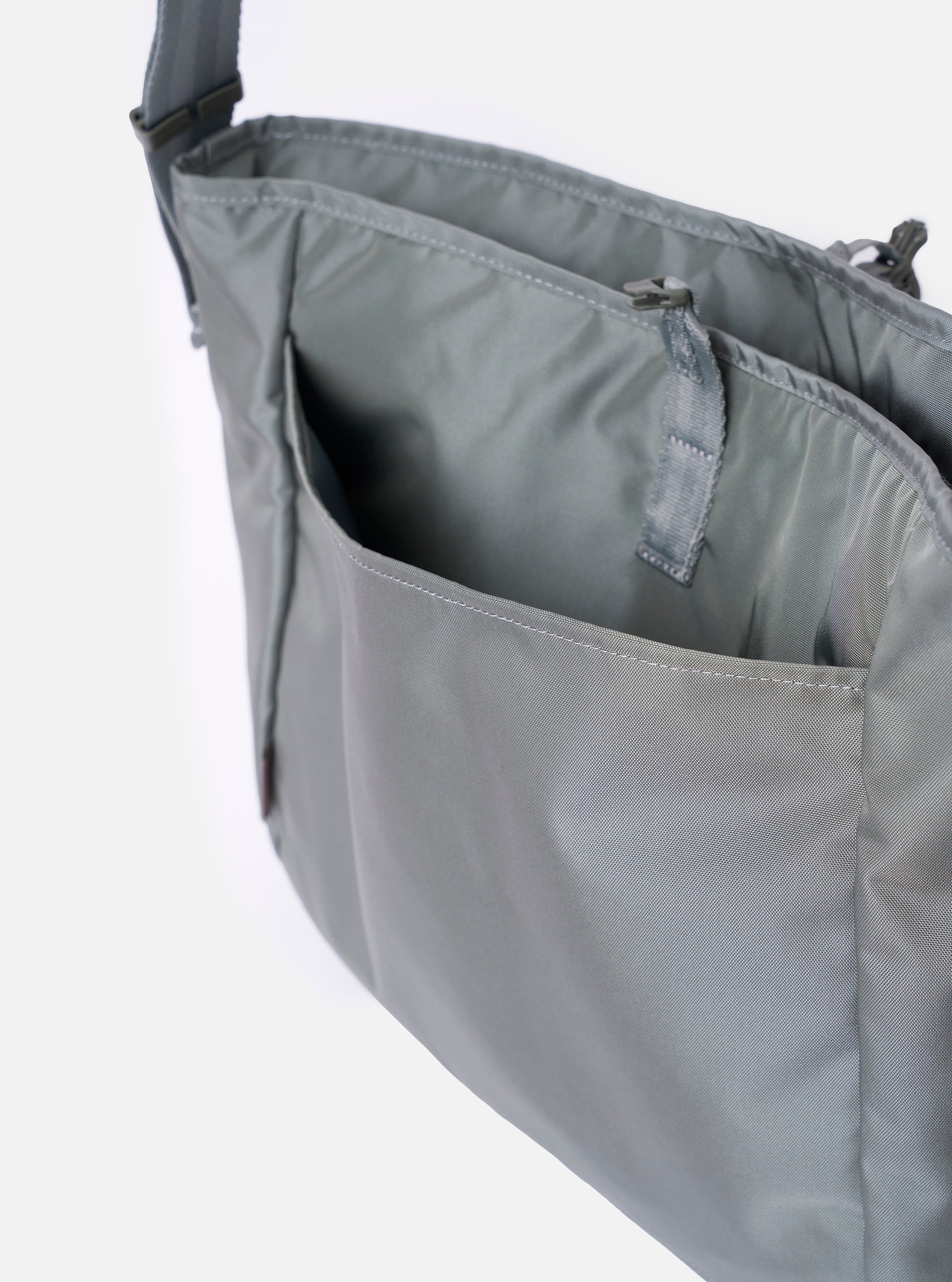 The F/CE.® Foliage Green Recycled Nylon 420 re/cor Courier Shoulder Bag is shown from a rear angle as a flat lay against a plain white background. The image highlights the adjustable messenger-style shoulder strap with a one-touch buckle and the structured, padded back panel. The foliage green recycled nylon fabric has a smooth, technical finish.