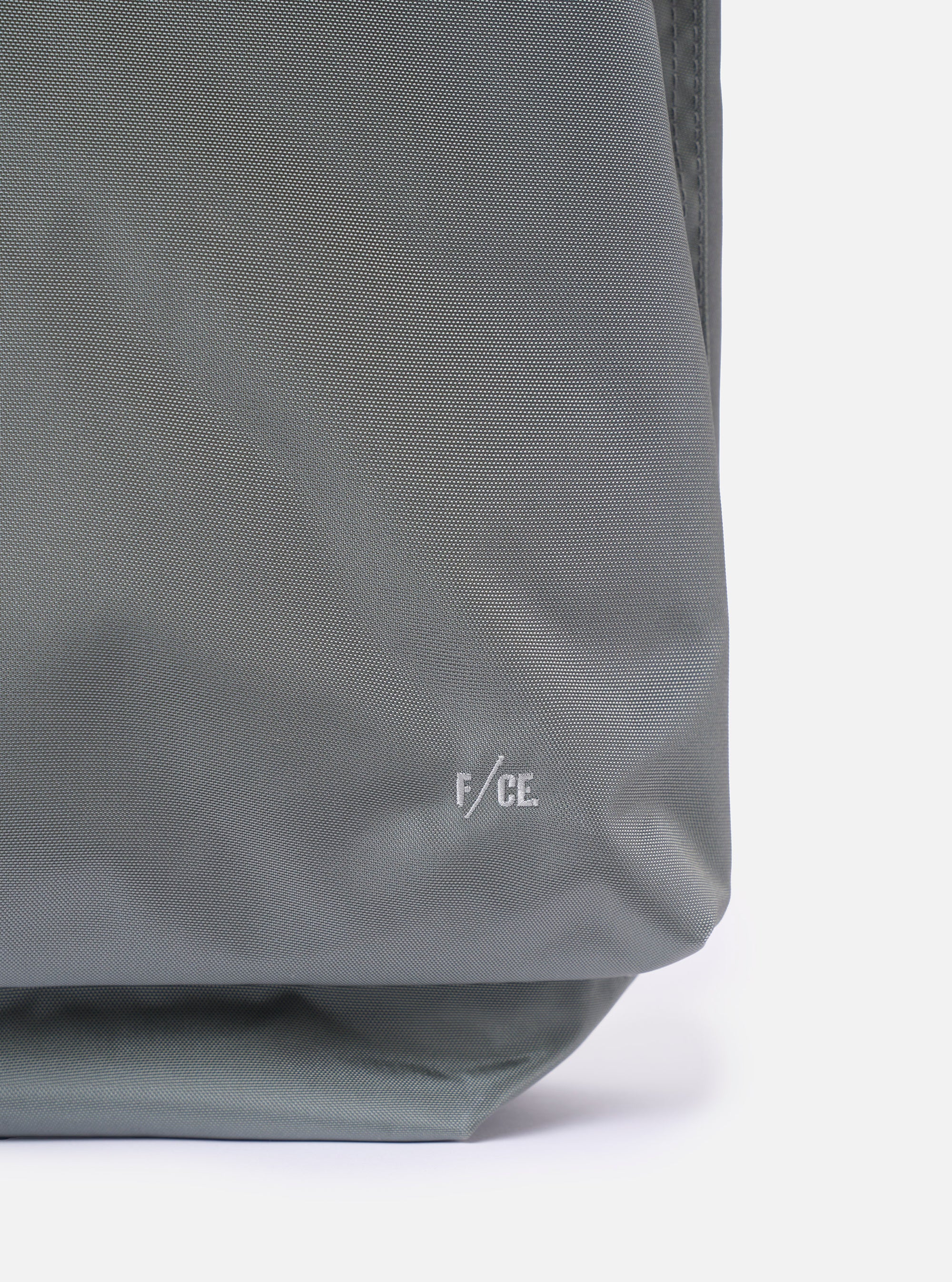 The F/CE.® Foliage Green Recycled Nylon 420 re/cor Courier Shoulder Bag is shown from a side-profile angle as a flat lay against a white background. The image highlights the depth and structured form of the messenger-style bag, featuring a foliage green technical fabric and a wide, adjustable black webbing shoulder strap.