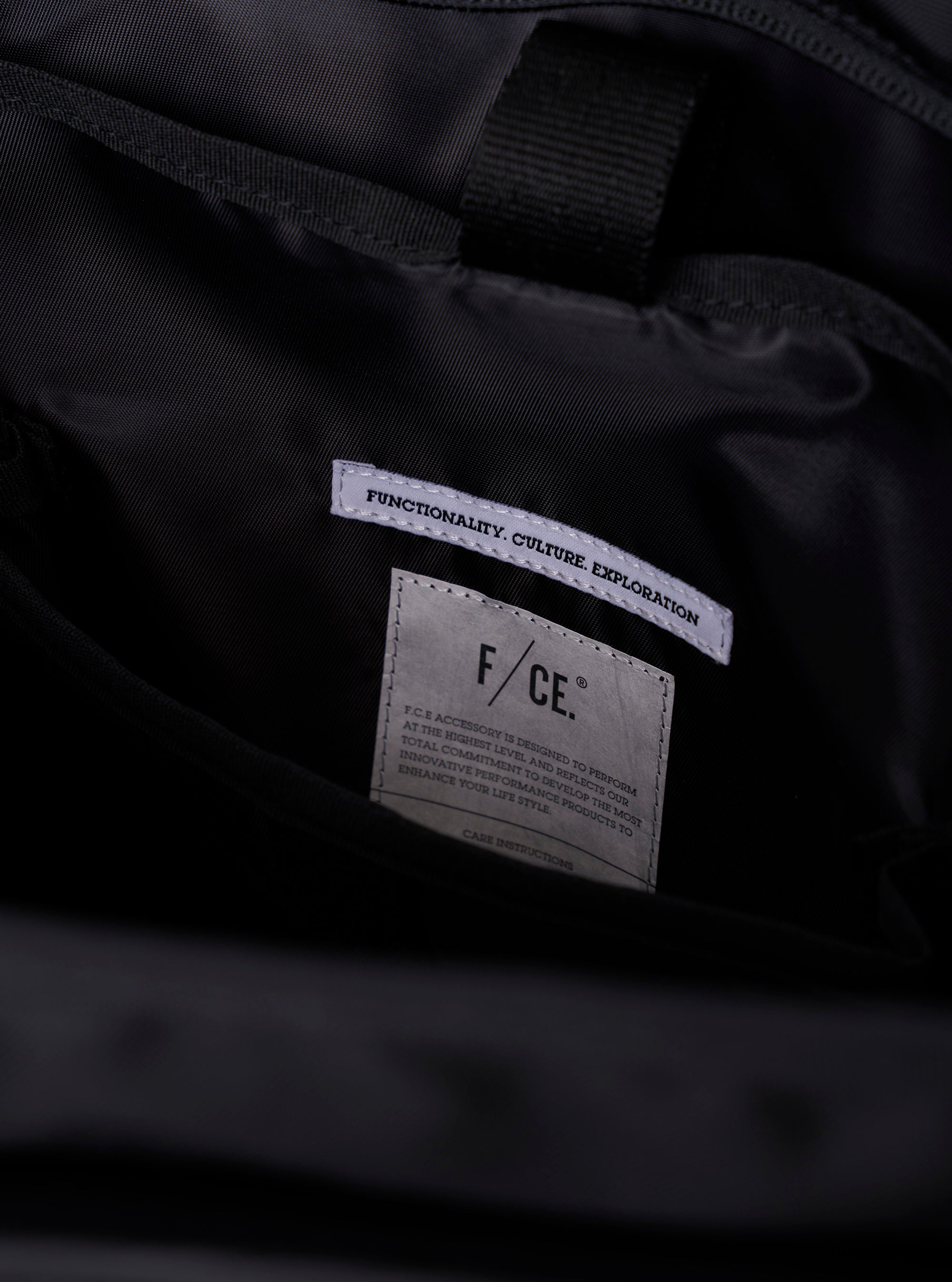 The F/CE. Black Recycled Nylon 420 re/cor Courier Shoulder Bag is shown from the back as it is worn by a model against a plain white background. The large black messenger-style bag features a wide, adjustable shoulder strap with a one-touch buckle mechanism and is positioned to fit snugly across the model's back. The bag is constructed from a smooth, recycled nylon fabric with a subtle sheen and visible tonal stitching. No mannequin is present in the image.