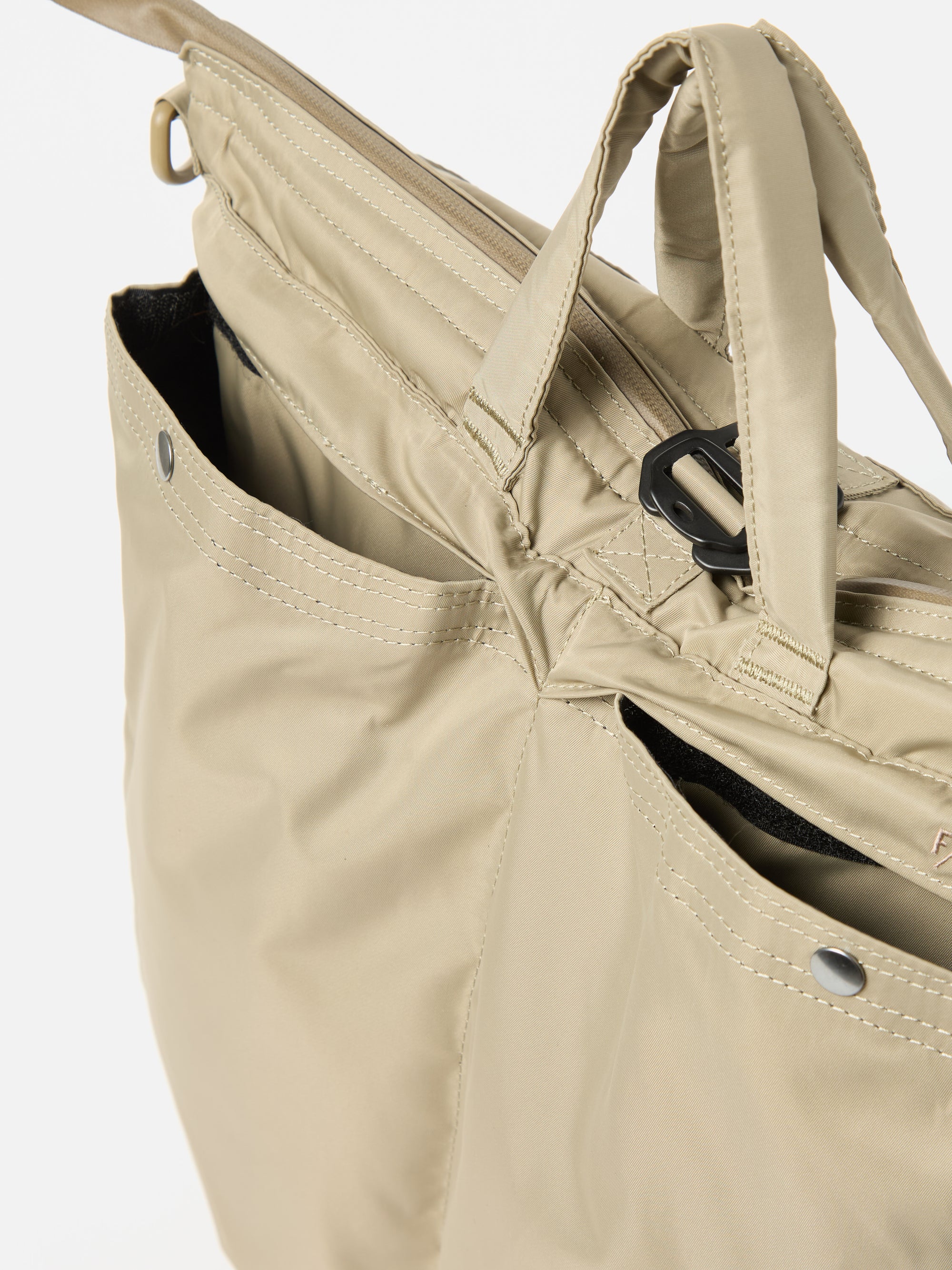 Close-up of the F/CE.® Sage Green Recycled Twill 3-Way Helmet Bag. The sage green bag, made of twill, features pockets with silver snap closures. Shot against a white backdrop.