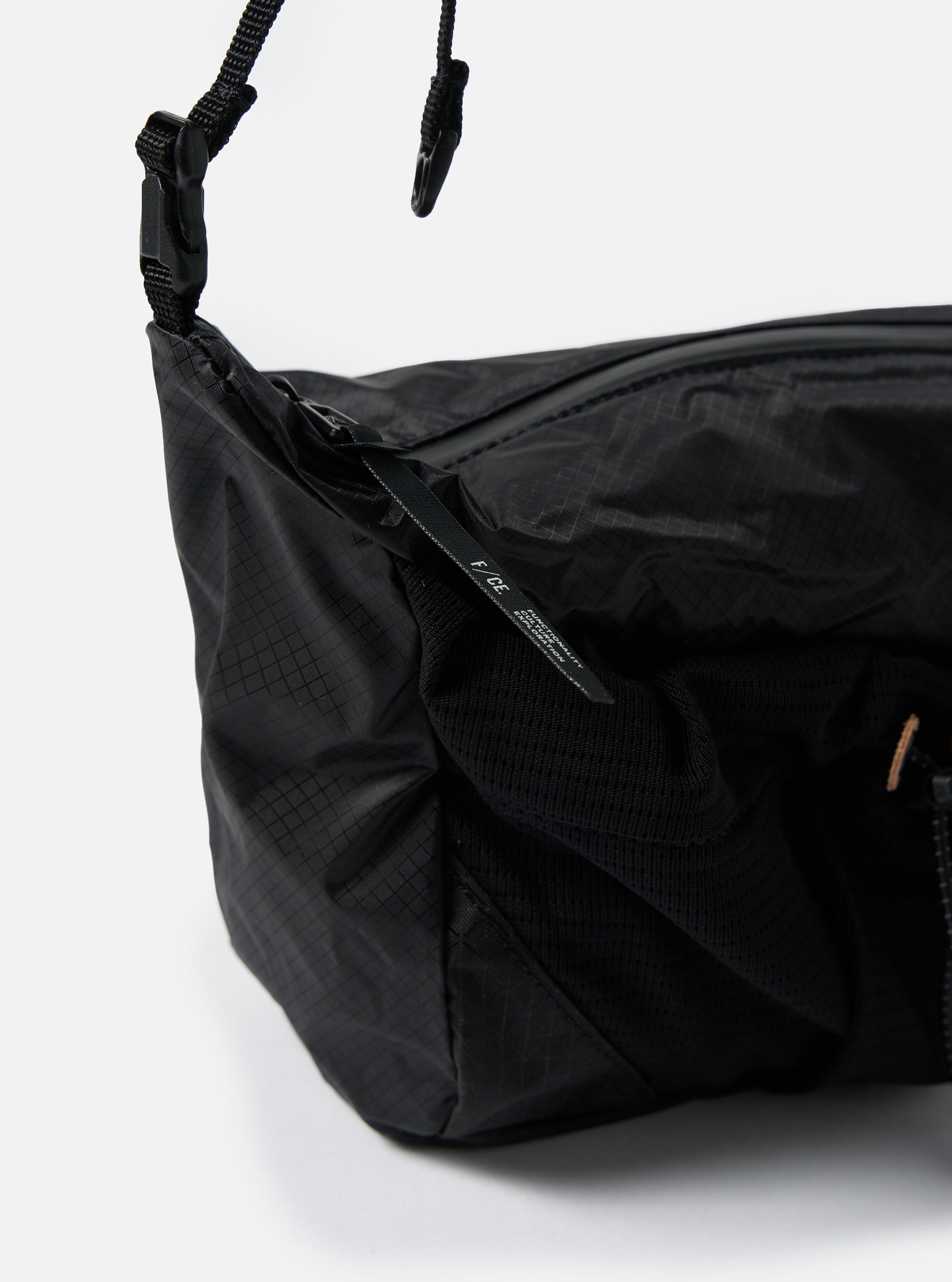 Close-up of the F/CE.® Black Nylon Cordura Sil Sacoche on a white background. The bag features a black nylon material with a grid pattern and a black strap.