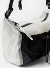 Close-up of the F/CE.® White Nylon Cordura Sil Sacoche against a white background. Features black straps and mesh, and a white tag. Shows the bag's texture and design details.