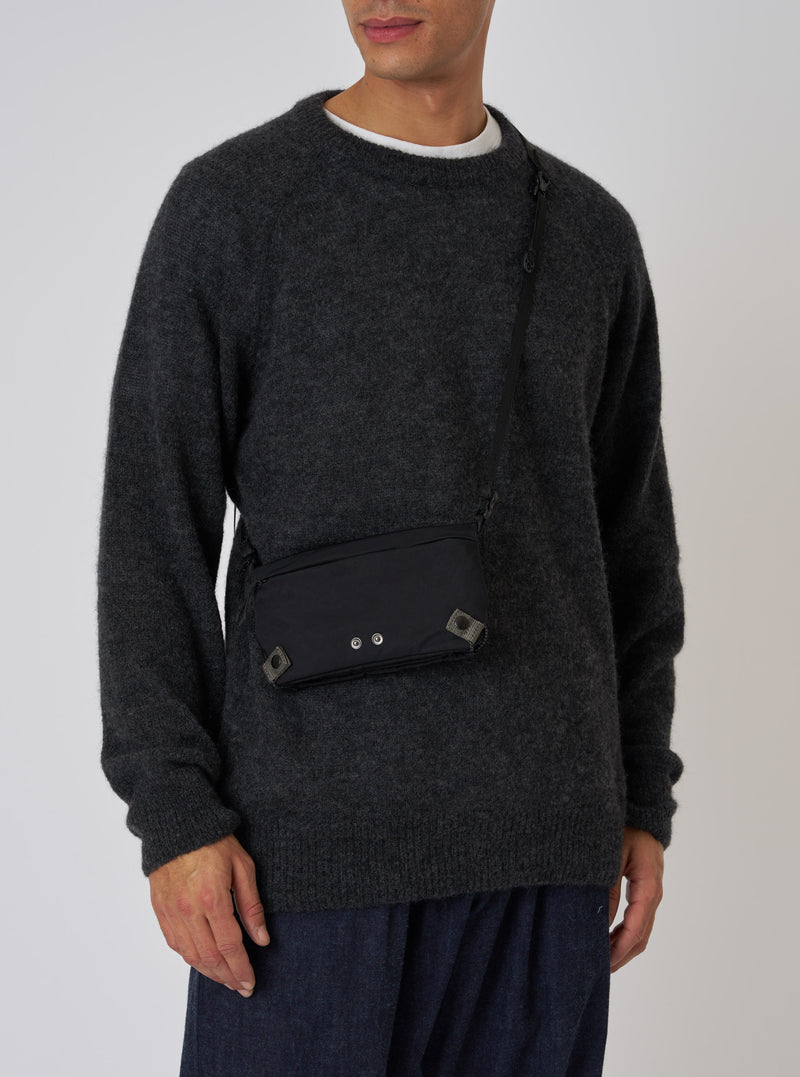 A model showcases the F/CE.® Black Nylon Textured Twill Drawstring Sacoche. The black bag is worn across the body. Shot against a plain background.