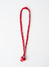 Hanami of Rome Red/Turquoise Bead Bandana Necklace No.49 on a white surface. The necklace is red with a turquoise bead at the bottom. The necklace is braided.