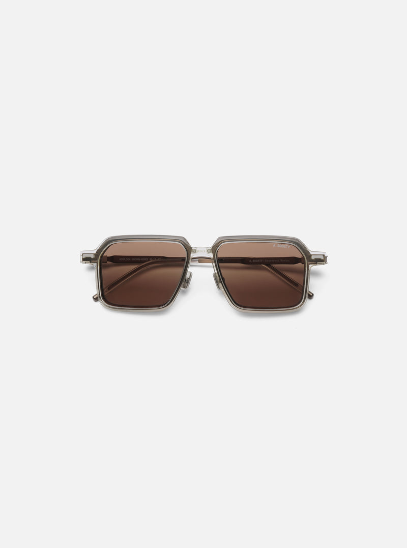 A. SOCIETY x Universal Works Kowloon Eyewear in brown and honey tones. Square frames with honey-colored lenses. Shot on a clean, white background.