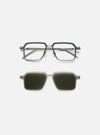 A. SOCIETY x Universal Works Olive/Green Kowloon Eyewear on a white surface. The glasses have an olive green frame and clear lenses, with a clip-on sunglass attachment.