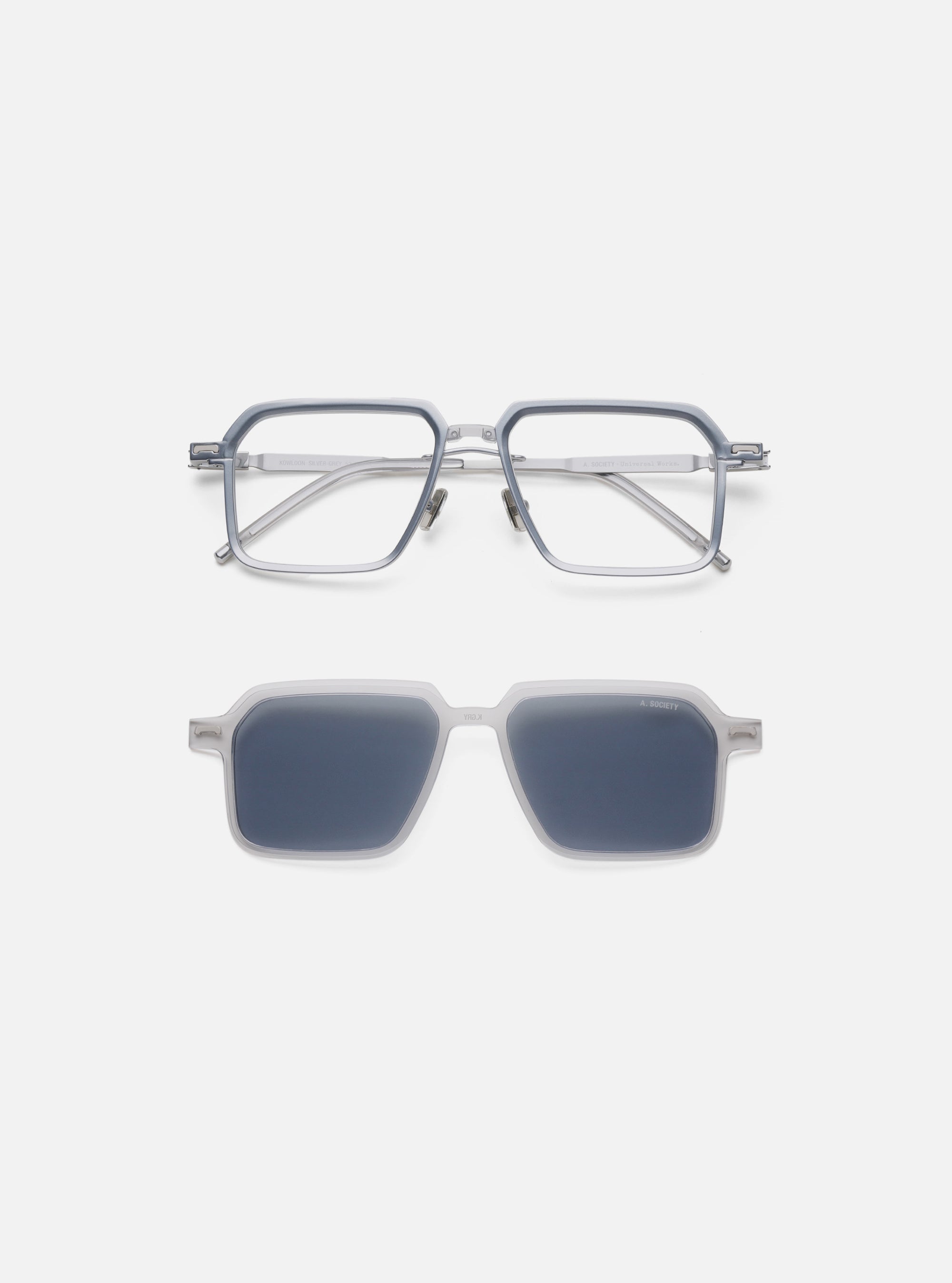 A. SOCIETY x Universal Works Silver/Grey Kowloon Eyewear on a white background. The frames are silver/grey. The sunglasses attachment has dark lenses.