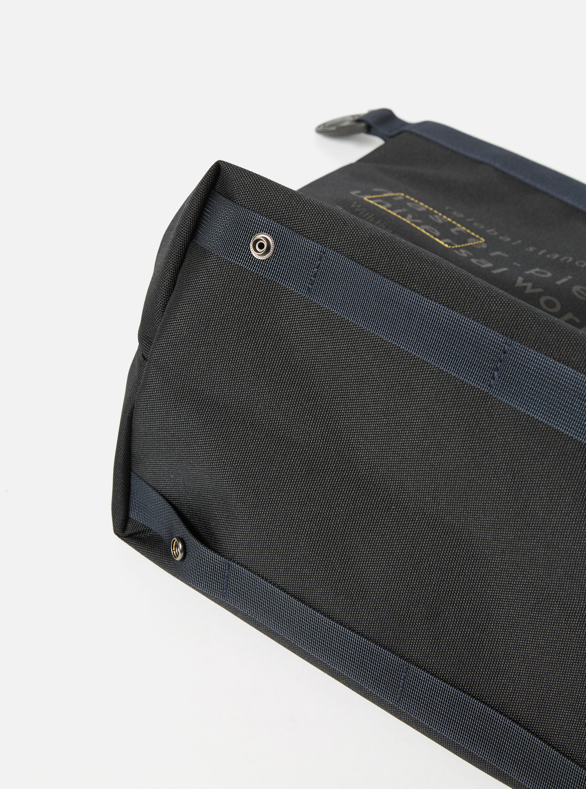 Close-up of the master-piece x Universal Works Black Recycled Tech Canvas Large Tote Bag. The black tech canvas material is visible with blue straps and silver rivets. Shot on a white background.