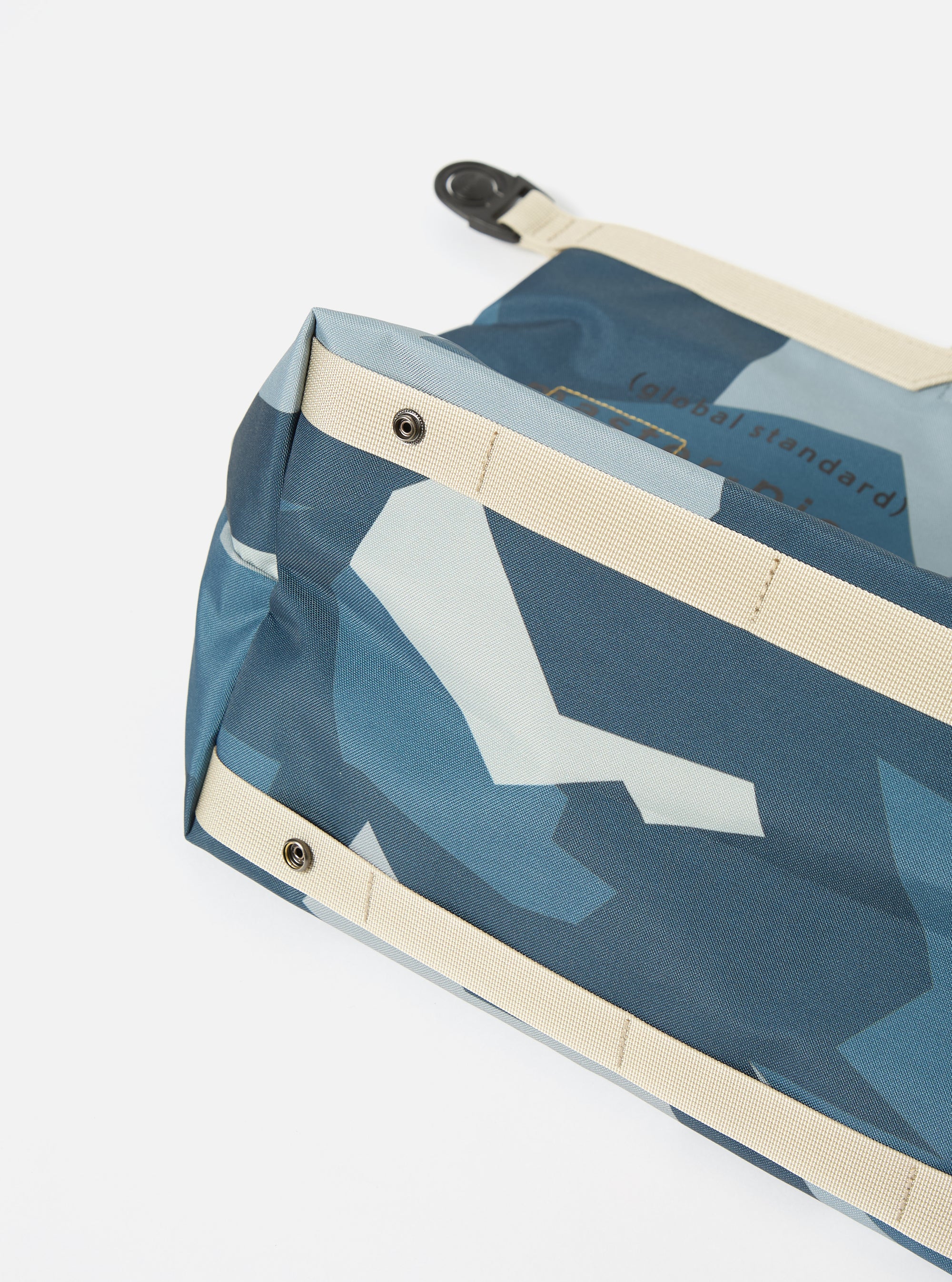 Close-up of a master-piece x Universal Works Blue Camo Recycled Tech Canvas Large Tote Bag on a white surface. The bag features a blue camo pattern and beige straps.