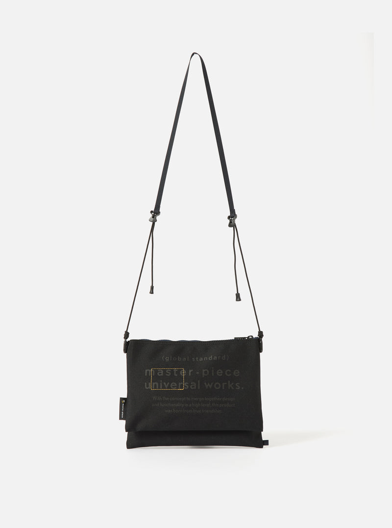 master-piece x Universal Works Black Recycled Tech Canvas Sacoche. Black canvas bag with adjustable strap on a white background. 