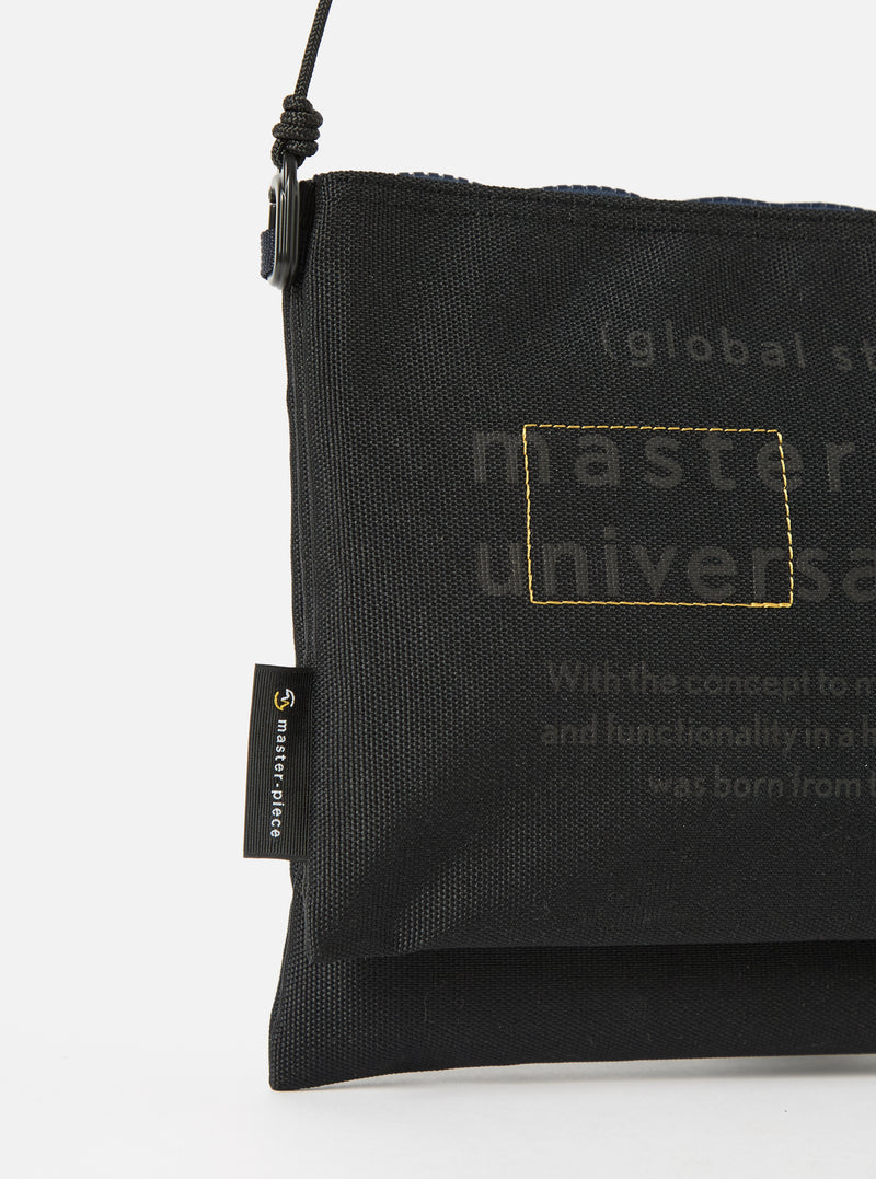 Close-up of the master-piece x Universal Works Black Recycled Tech Canvas Sacoche on a white background. The black canvas bag features subtle branding details.