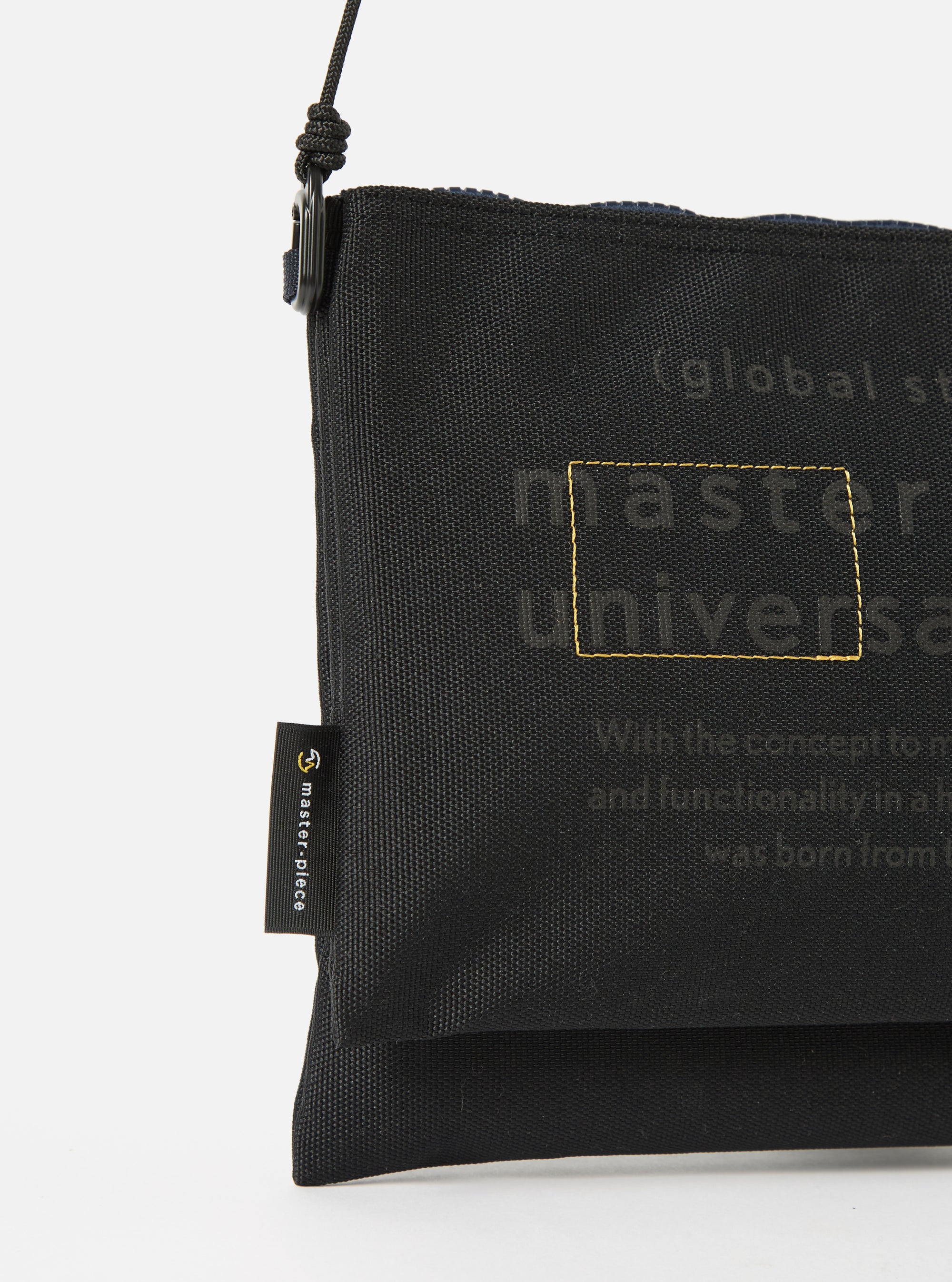 Close-up of the master-piece x Universal Works Black Recycled Tech Canvas Sacoche on a white background. The black canvas bag features subtle branding details.