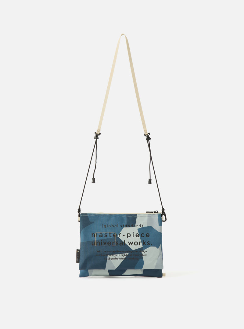 master-piece x Universal Works Blue Camo Recycled Tech Canvas Sacoche on a white background. The bag has a blue camo pattern and a beige strap.