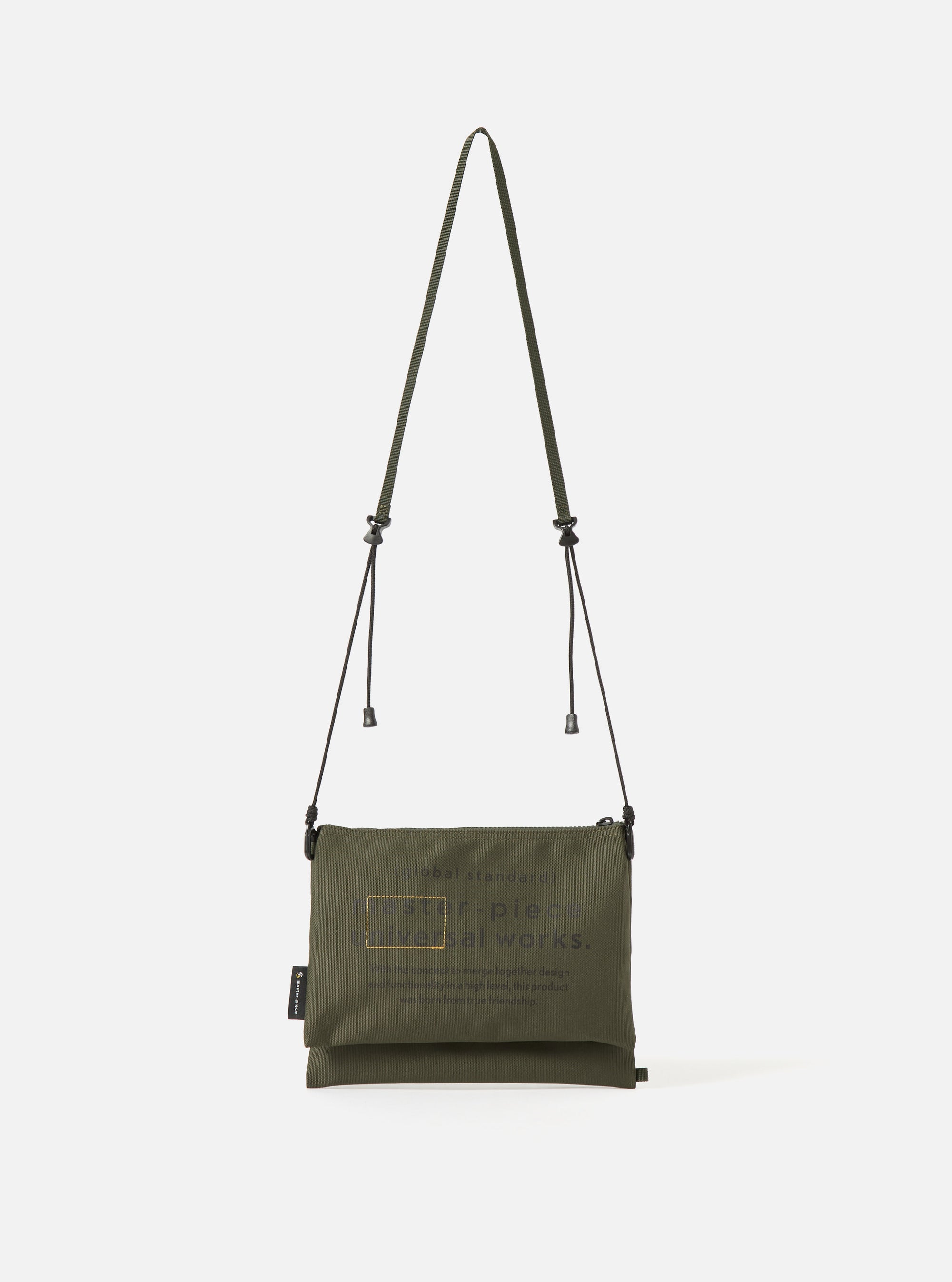 master-piece x Universal Works Olive Recycled Tech Canvas Sacoche on a clean white background. The olive green bag features black drawstrings and subtle branding.