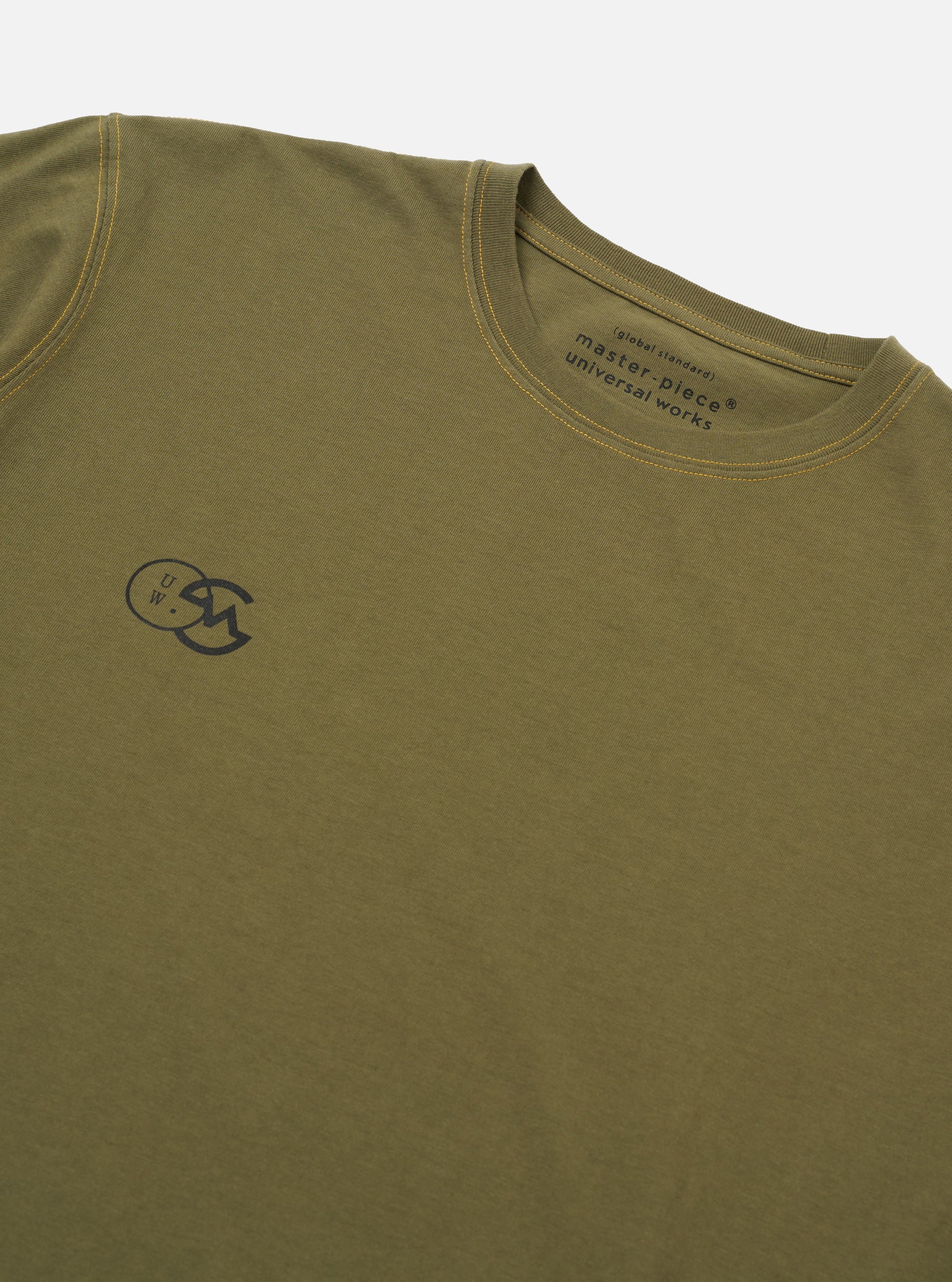 The master-piece x Universal Works Olive Single Jersey Print Tee is shown as a flat lay against a white background. The image displays the back of the olive green t-shirt, featuring a large graphic print of a geometric mountain landscape in orange and black. The garment has short sleeves and a ribbed crew neck.