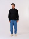 The master-piece x Universal Works Black Peached Poplin Newark Jacket is shown as a flat lay against a white background. The jacket features a ribbed bomber-style collar, a full zip and snap-button front closure, two large slanted hand pockets, and a zippered stash pocket on the left sleeve. It includes collaborative branding badges on the chest.