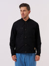 A model wears the master-piece x Universal Works Black Peached Poplin Newark Jacket over a dark top, standing against a plain white background. The jacket is a bomber-style design featuring a ribbed collar, cuffs, and hem, with a central zip closure and slanted side pockets. The fabric has a soft, matte finish characteristic of peached poplin. Dual branding is visible on the chest.