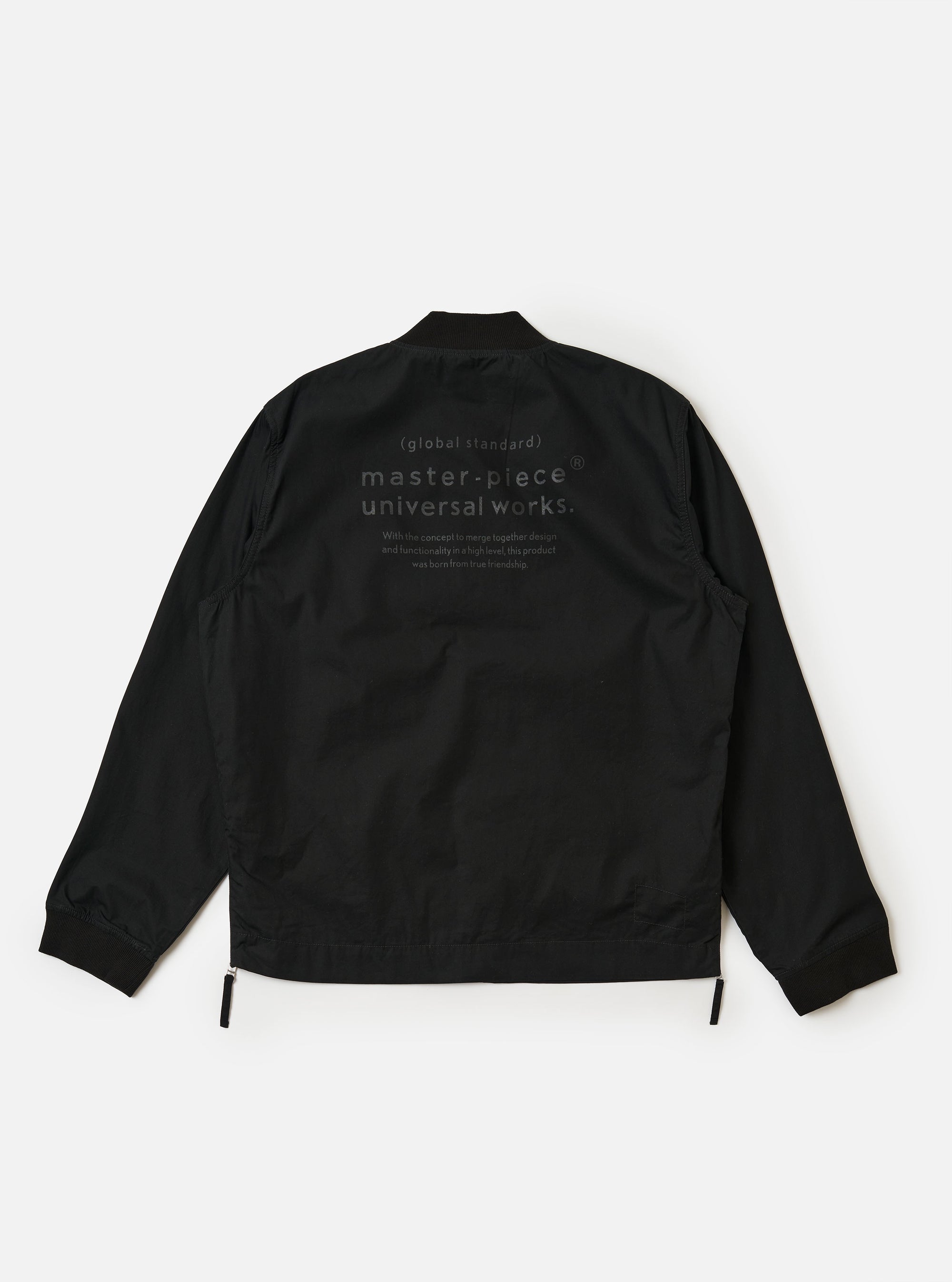 The master-piece x Universal Works Black Peached Poplin Newark Jacket is shown from the back as a flat lay against a plain white background. The image highlights the smooth texture of the black peached poplin fabric, the ribbed collar, and the ribbed hem. A small collaborative brand patch is visible on the upper back.